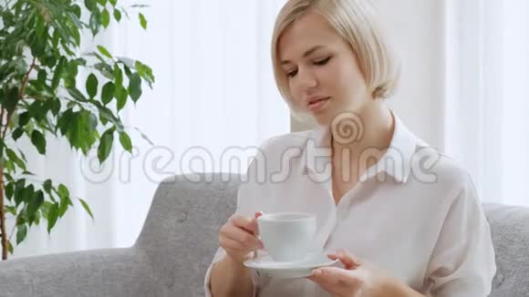 一个年轻漂亮的金发女人带着眼镜在一间清淡的公寓里喝着白色杯子里的咖啡视频的预览图