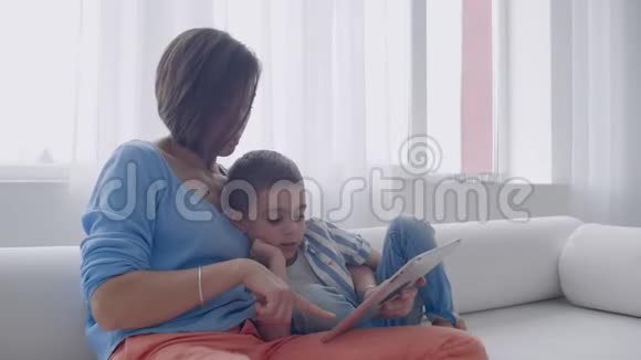 快乐的妈妈和小儿子早上一起在家客厅看书家庭活动概念视频的预览图