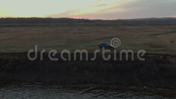 越野黑色SUV车行驶在河岸上金色的日落景观晚上沿海水沿海岸骑逾越节车视频的预览图
