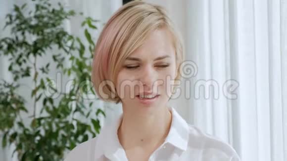 一个年轻漂亮的金发女人带着眼镜在一间清淡的公寓里喝着白色杯子里的咖啡视频的预览图