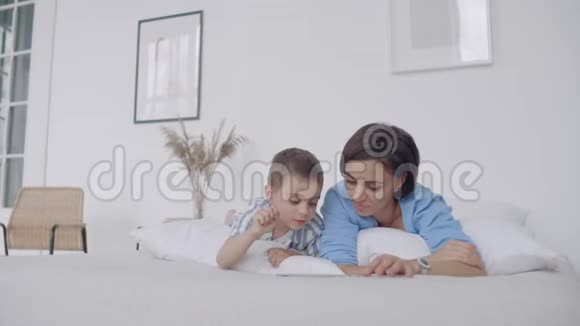 母亲和儿子在家里的卧室里使用数字平板电脑用数字显示快乐白人母子的正面观点视频的预览图
