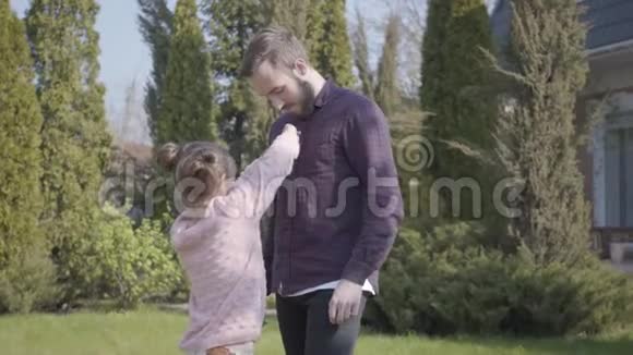 小女孩试图扣父亲站在户外的衬衫家庭休闲户外春天聚会视频的预览图