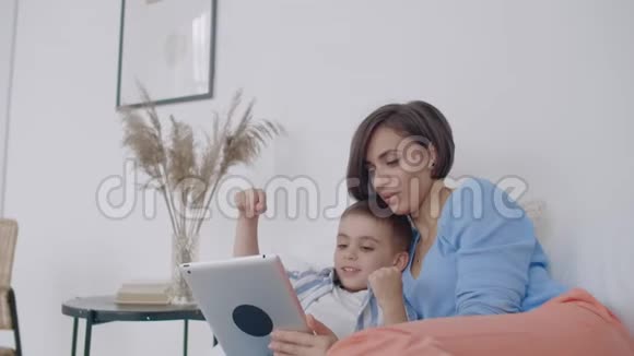 母子俩看着躺在白色床上的平板屏幕在平板电脑上和你儿子玩游戏视频的预览图