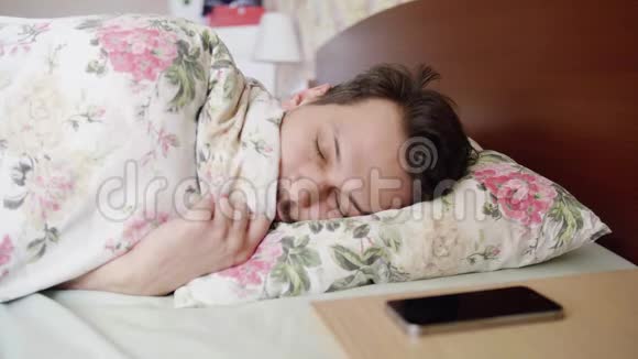 男人睡在床上有舒适的枕头和毯子电话铃声他醒来视频的预览图