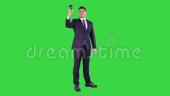 快乐年轻英俊的商人用他的手机在绿色屏幕上录制vlogChroma键视频的预览图