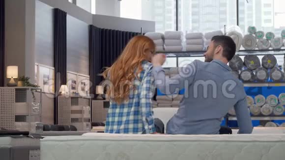 一对夫妇拥抱的后景镜头坐在家具店的一张新床上视频的预览图