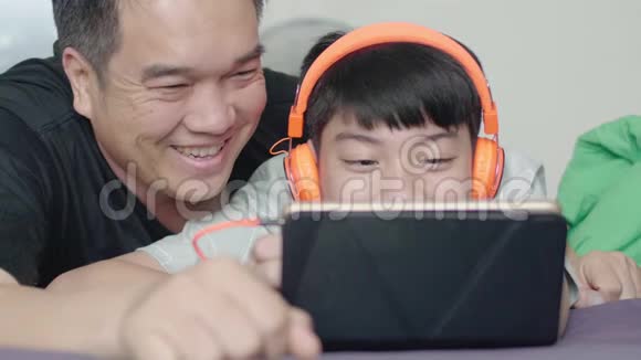 父亲和儿子在家里带着笑脸在平板电脑上欣赏电影视频的预览图