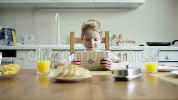 高兴的男孩坐在午餐时用平板电脑和流动相机在上面玩视频的预览图