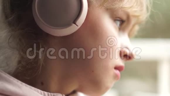窗户边一个戴着粉红色耳机的女孩的肖像女学生听音乐很伤心视频的预览图