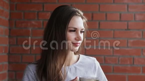 美女端着一杯热茶一个女孩在砖墙上喝茶视频的预览图