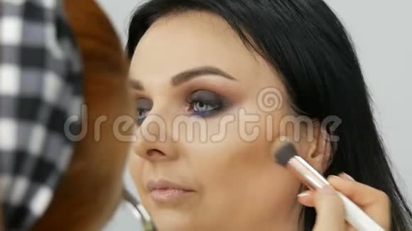 化妆师带着一个女人的脸用刷子涂粉粉底或遮瑕膏丁香和珍珠视频的预览图