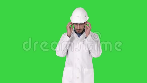 年轻的工程师穿着长袍和头盔戴着眼镜在绿色屏幕上行走Chroma键视频的预览图