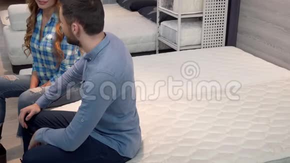 可爱的幸福夫妇躺在家具店舒适的床褥上视频的预览图