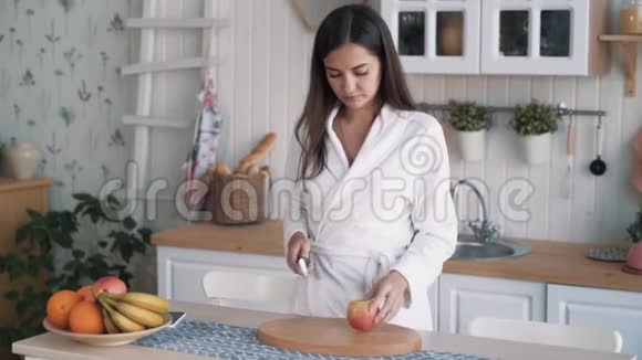 穿着浴袍的可爱女孩拿着苹果放在船上切在厨房里慢动作视频的预览图