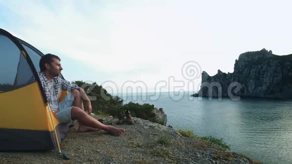 一个年轻人坐在帐篷里在智能手机上拍照拍摄美丽的海洋景观视频的预览图