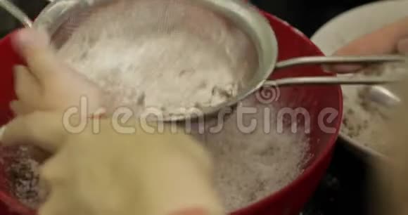 母亲和女儿双手将可可粉放入盛有面粉的碗中视频的预览图