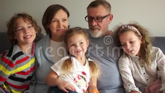 一个幸福的大家庭的亲密肖像祖父母正坐在沙发上拥抱他们的三个孙子视频的预览图