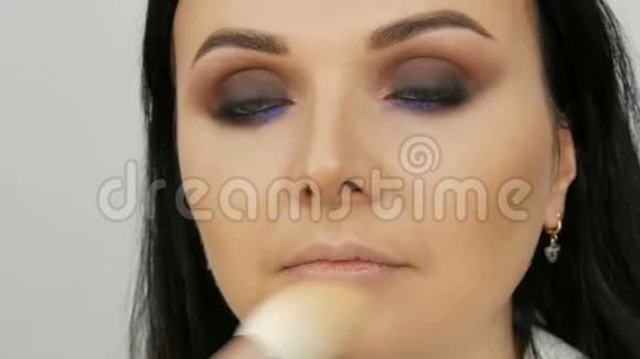 化妆师带着一个女人的脸用刷子涂粉粉底或遮瑕膏丁香和珍珠视频的预览图