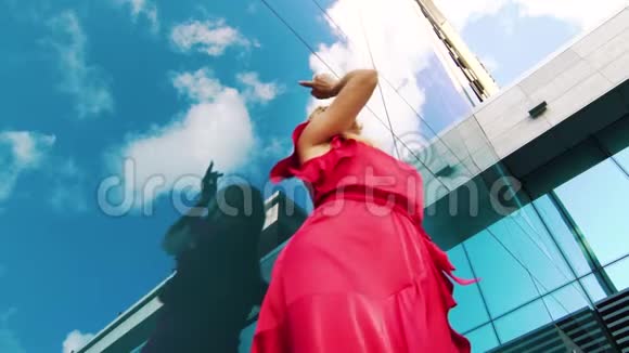 年轻女子在摩天大楼反射面附近跳舞的低角度镜头视频的预览图