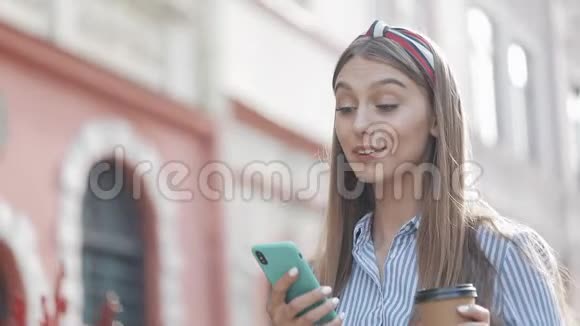 可爱的女人穿着蓝色和白色条纹连衣裙使用智能手机上的应用程序在旧城街道上行走美丽美丽视频的预览图