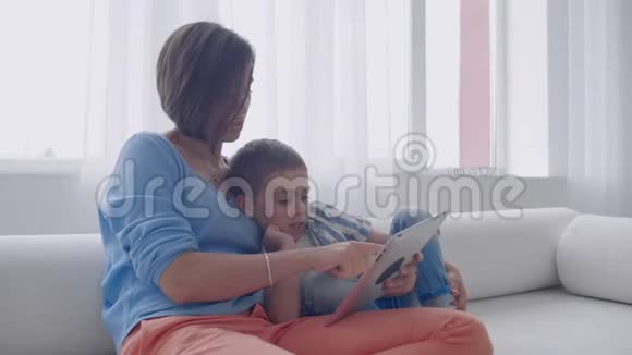 幸福的家庭妈妈和孩子儿子坐在沙发上用数码平板电脑微笑的父母和孩子的儿子抱着电脑视频的预览图