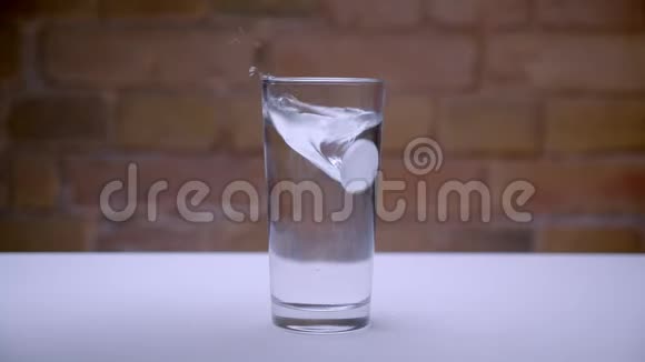 白色桌子上的透明玻璃特写镜头水和药丸被扔进桌子里视频的预览图