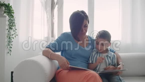 母子俩读书快乐的年轻母子在家的沙发上看书视频的预览图