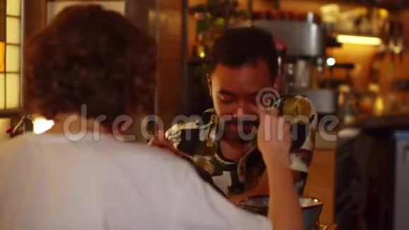 两个年轻人坐在咖啡馆的桌子旁他们吃食物交谈友好视频的预览图