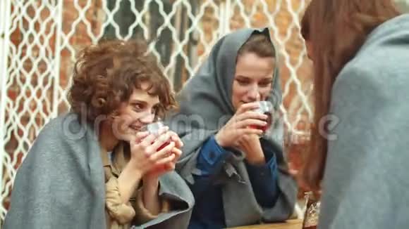 穿着毯子的女孩坐在咖啡馆外面喝热茶聊天视频的预览图