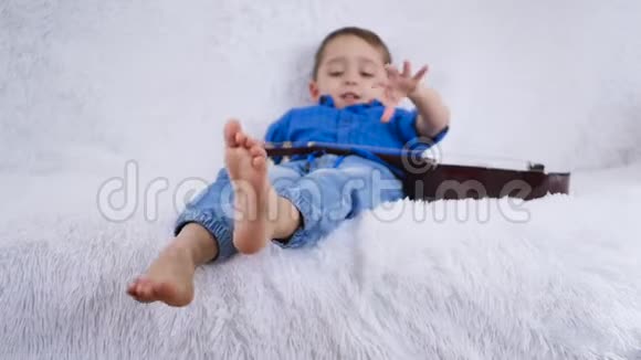 一个拿着吉他的孩子躺在白色的沙发上摸着吉他的琴弦视频的预览图
