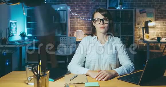 一位戴眼镜的漂亮女士在办公室的办公桌上看着相机视频的预览图