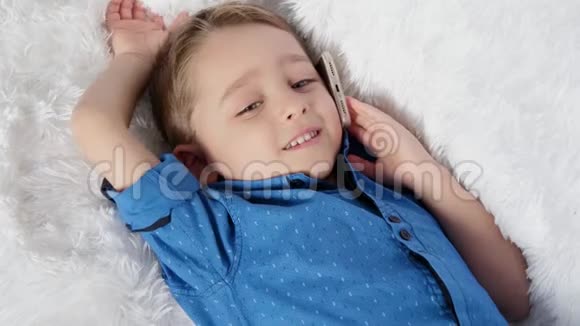 一个可爱的孩子躺在白色的沙发上打着电话体验着真挚的情感快乐幸福欢笑视频的预览图