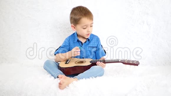 一个快乐的男孩坐在白色的沙发上拿着吉他玩得很开心笑着挥舞着手臂表现得很积极视频的预览图