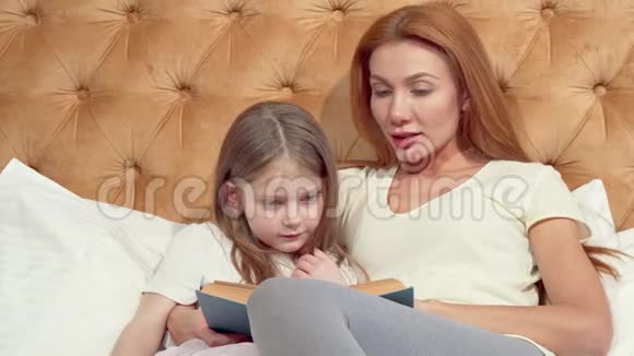 可爱的小女孩和她美丽的妈妈对着镜头微笑读着一本书视频的预览图