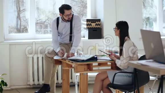 快乐轻松的年轻男性老板商人与坐在现代阁楼办公室工作场所桌子上的女性同事交谈视频的预览图