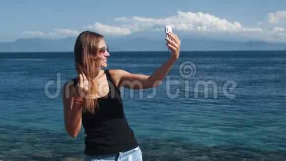 戴墨镜的快乐女旅行者在手机上自拍背景是海洋视频的预览图