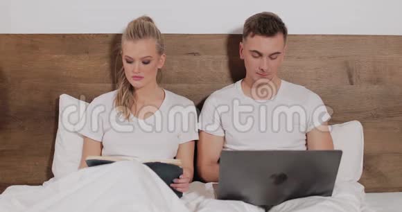 女孩阅读书籍而男人使用笔记本电脑床视频的预览图
