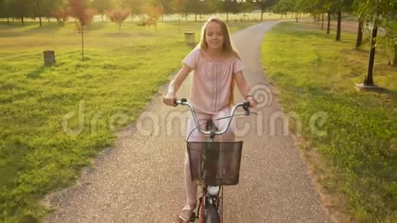 女孩骑自行车在公园的小巷里迎着夕阳视频的预览图