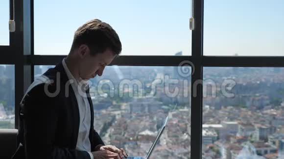 穿西装的Ofiice工人正在坐在窗户附近的笔记本电脑上打字可以看到城市全景视频的预览图
