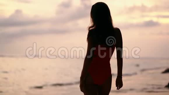 穿着泳装的剪影女孩看日落看海滩上的海洋慢动作视频的预览图