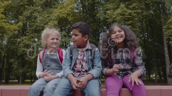 回学校去三个朋友背包拥抱和笑在学校附近学校儿童混合种族团体视频的预览图
