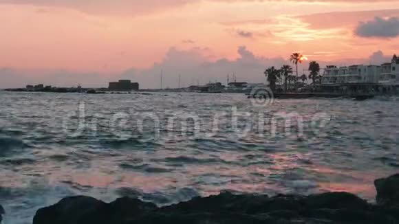 红色日落有暴风雨的大海码头长廊和地平线上的城堡塞浦路斯帕福斯日落时太阳路和海浪撞击岩石视频的预览图