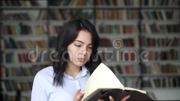 在图书馆书架的背景下一位年轻女性正在阅读一本书视频的预览图