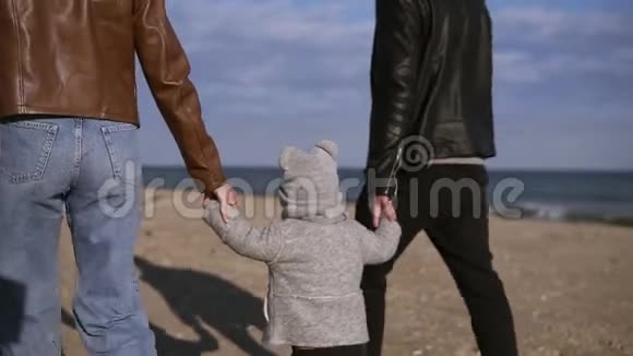 时尚年轻的父母带着儿子走在中间正走在秋天春天的海边手握双手视频的预览图
