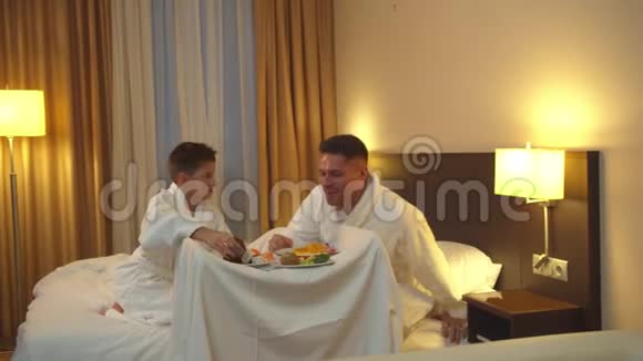 父子俩坐在旅馆房间的床上吃着食物视频的预览图