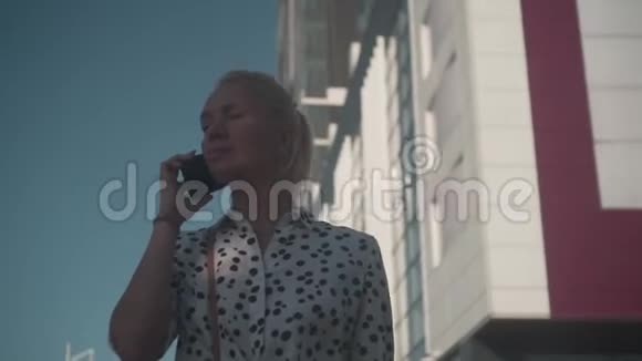 商务女性穿着一件白色衬衫上面挂着豆站在现代办公楼附近打电话视频的预览图
