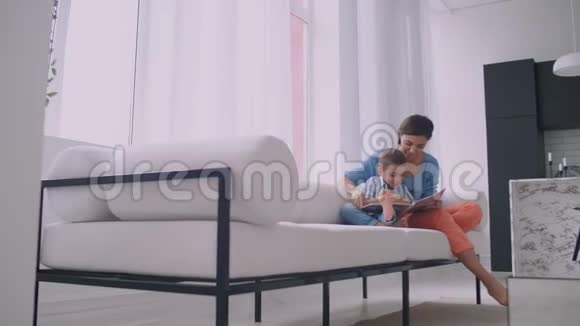 母子俩读书快乐的年轻母子在家的沙发上看书视频的预览图