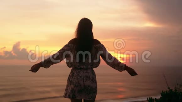 女孩张开双臂的剪影矗立在悬崖上背景上是日落慢动作视频的预览图