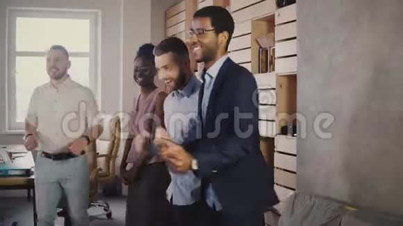 快乐的非裔美国人高管与同事在休闲办公室聚会上跳舞庆祝商业成就4K视频的预览图