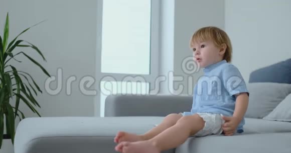 一个2岁的男孩坐在沙发上看电视手里拿着遥控器看动画片和电视视频的预览图